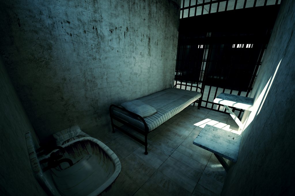 Render of locked old prison cell for one person with bed, sink, toilet and chair. Dark atmosphere.